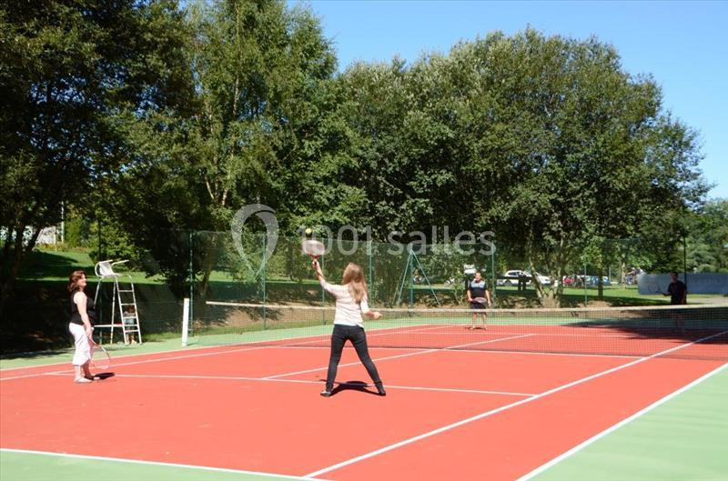 Deux personnes jouent au tennis sur un court extérieur entouré d'arbres par une journée ensoleillée.