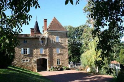Allée rouge bordée de plantes et de panneaux, menant à une maison en pierre sous un ciel dégagé.