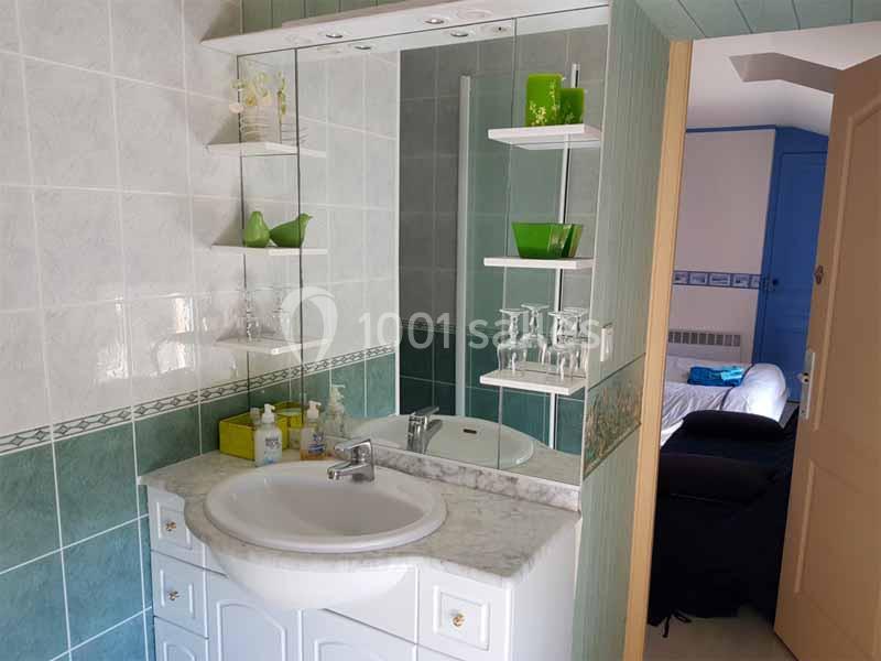 Lavabo avec miroir entouré d'étagères contenant des objets verts, dans une salle de bain carrelée.