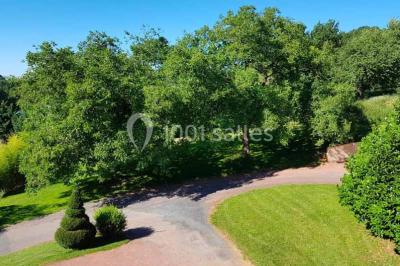 Allée rouge bordée de plantes et de panneaux, menant à une maison en pierre sous un ciel dégagé.
