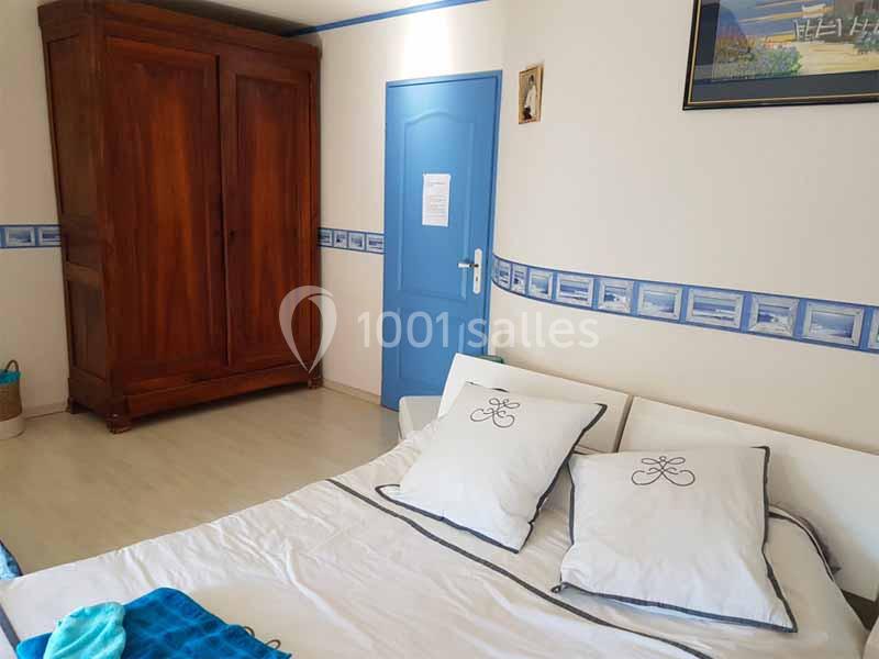 Chambre lumineuse avec lit double, armoire en bois, porte bleue et décoration murale sobre.