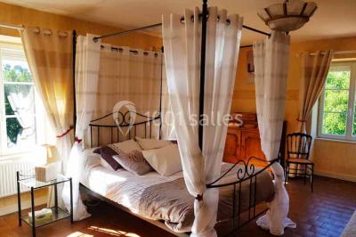 Allée rouge bordée de plantes et de panneaux, menant à une maison en pierre sous un ciel dégagé.