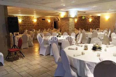 Allée rouge bordée de plantes et de panneaux, menant à une maison en pierre sous un ciel dégagé.
