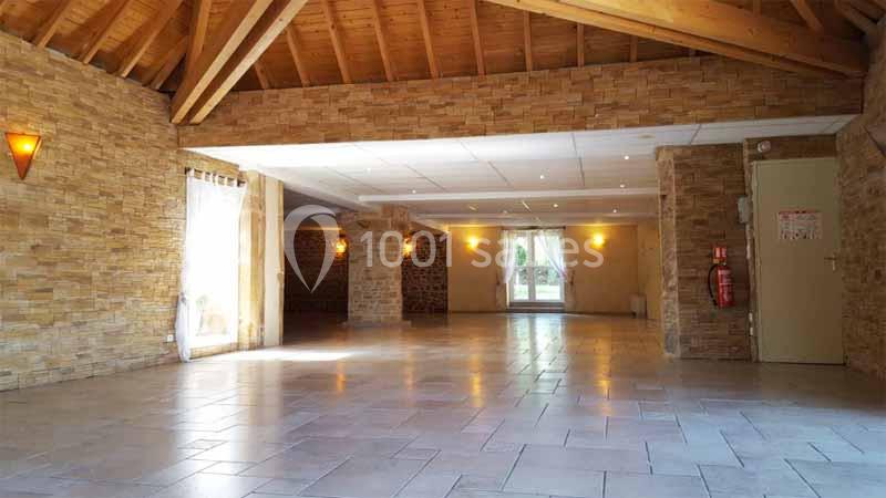 Salle spacieuse avec murs en pierre, plafond en bois et grandes ouvertures laissant entrer la lumière naturelle.