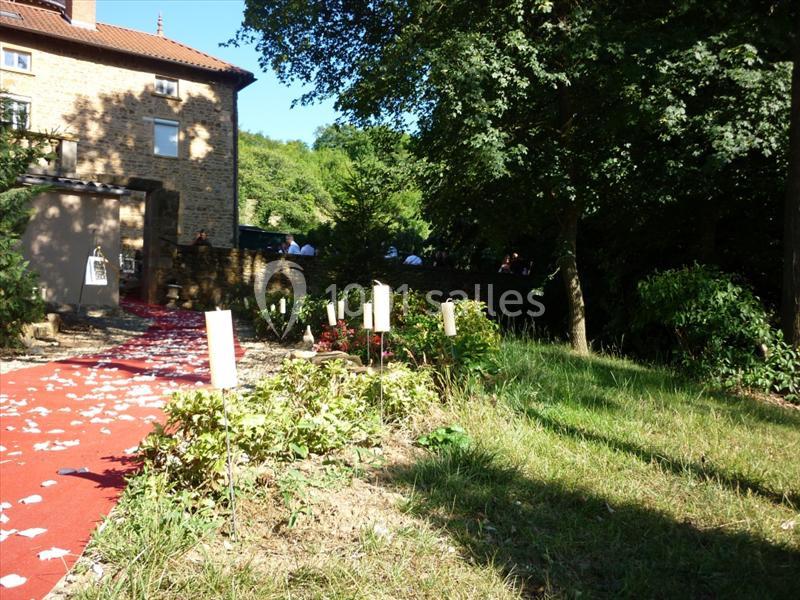 Allée rouge bordée de plantes et de panneaux, menant à une maison en pierre sous un ciel dégagé.