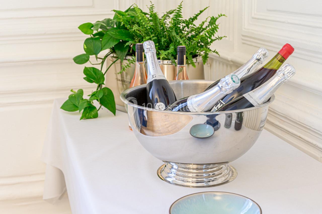 Des bouteilles de vin et de champagne dans un seau en métal, posées sur une table avec des plantes en arrière-plan.