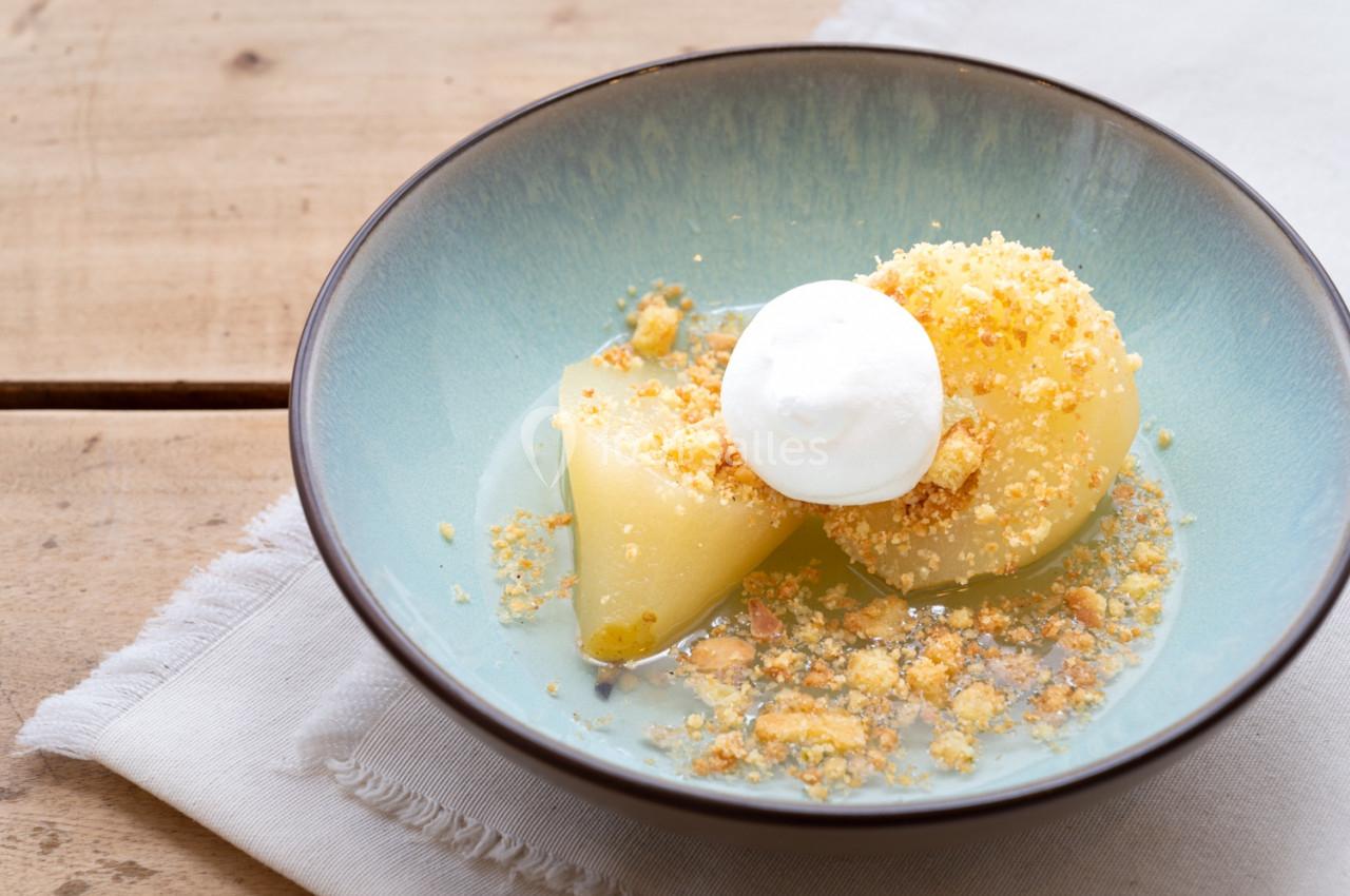 Poires pochées servies avec une crème fouettée et des éclats de biscuits dans une assiette bleue sur une table en bois.