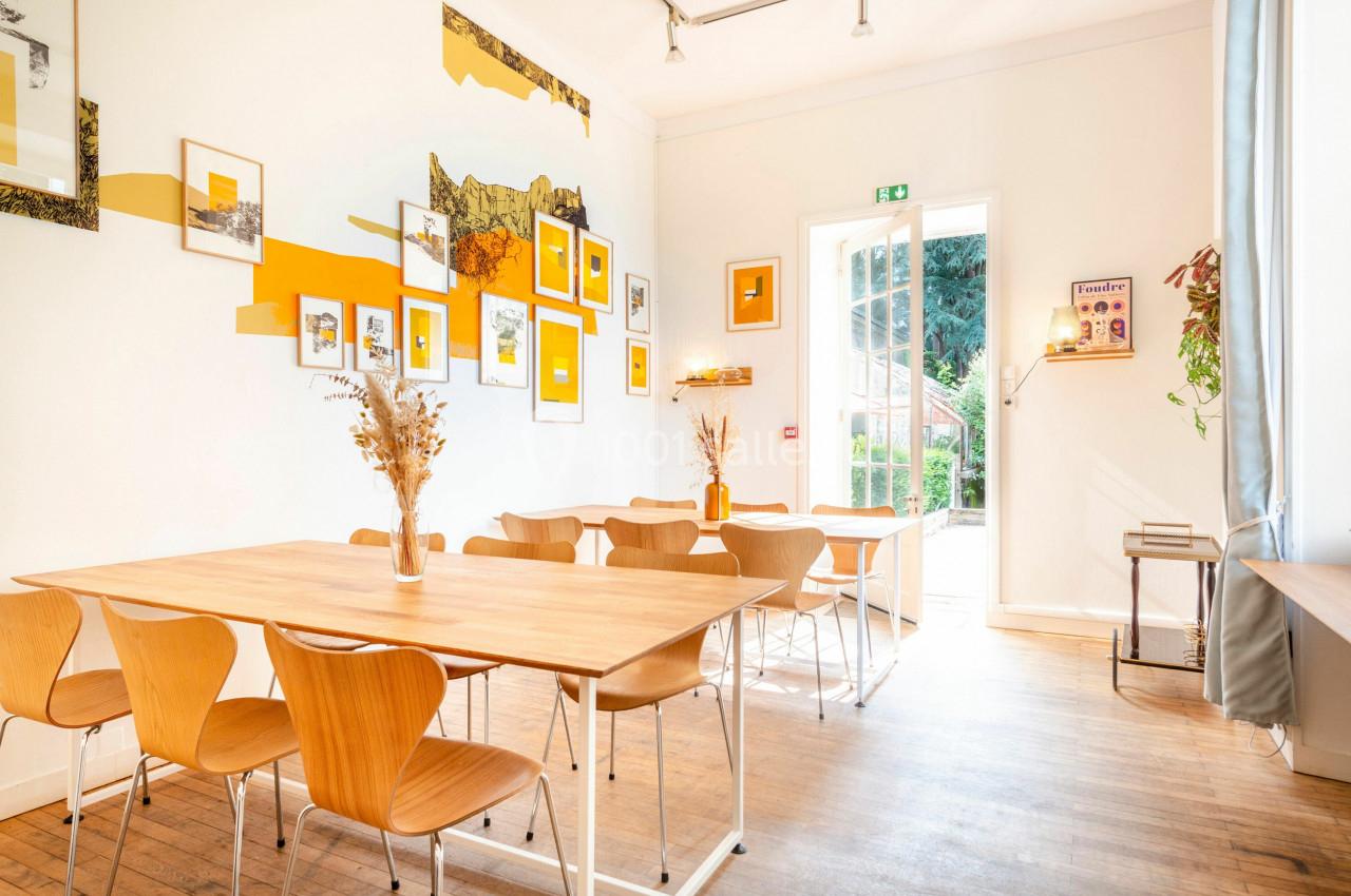 Salle lumineuse avec tables en bois, chaises assorties, décorations murales colorées et porte ouverte sur un jardin.