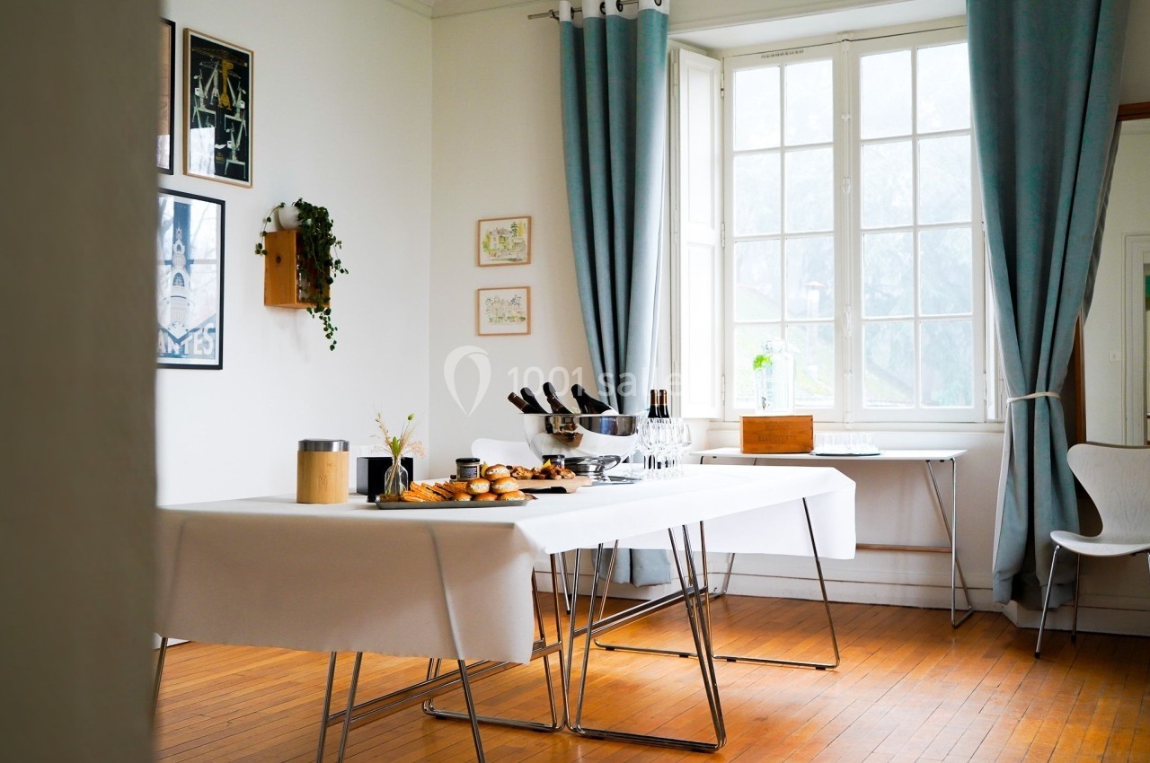 Table dressée dans une pièce lumineuse avec des rideaux bleus, des cadres au mur et des viennoiseries disposées.