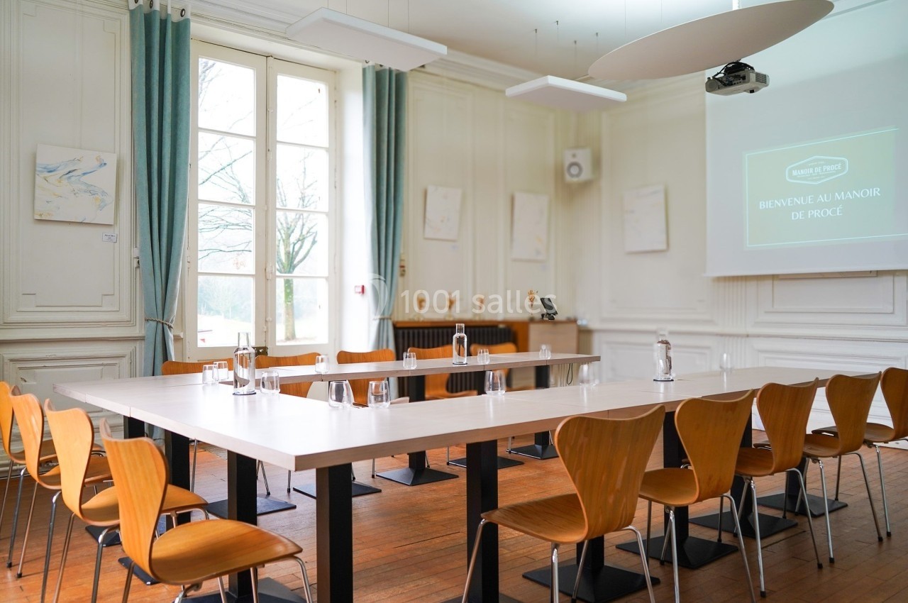 Salle de réunion lumineuse avec tables en U, chaises en bois, écran de projection et grandes fenêtres donnant sur l…