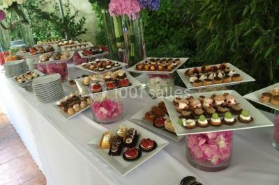 Salle décorée pour un événement, avec des tables rondes dressées, chaises rouges et un fond floral rose.