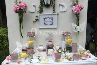 Salle décorée pour un événement, avec des tables rondes dressées, chaises rouges et un fond floral rose.