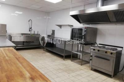 Salle décorée pour un événement, avec des tables rondes dressées, chaises rouges et un fond floral rose.