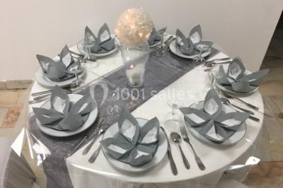 Salle décorée pour un événement, avec des tables rondes dressées, chaises rouges et un fond floral rose.