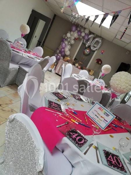 Salle décorée pour une fête d'anniversaire avec des tables dressées, des ballons et une arche festive.