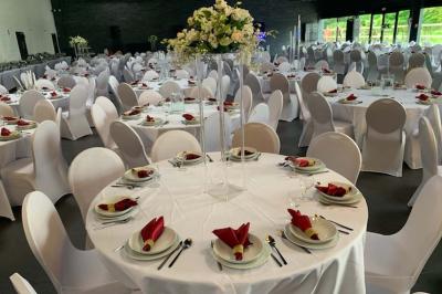 Salle décorée pour un événement, avec des tables rondes dressées, chaises rouges et un fond floral rose.