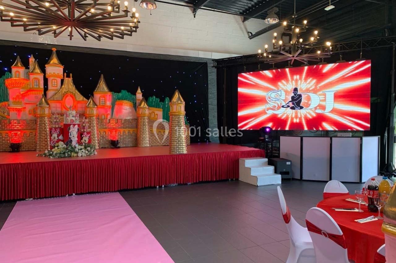 Décor de fête avec château miniature illuminé, scène rouge, écran affichant ’S&DJ’ et tables décorées en premier plan.