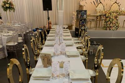 Salle décorée pour un événement, avec des tables rondes dressées, chaises rouges et un fond floral rose.
