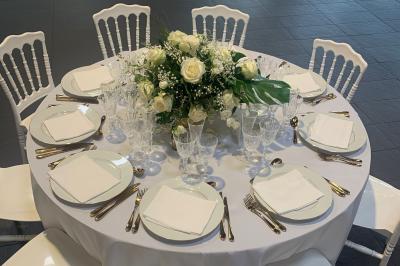 Salle décorée pour un événement, avec des tables rondes dressées, chaises rouges et un fond floral rose.