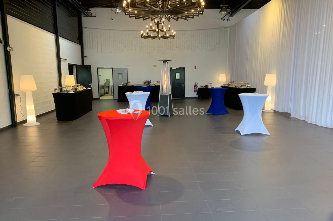 Salle de réception moderne avec tables hautes colorées, buffet en arrière-plan et éclairage suspendu.