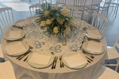 Salle décorée pour un événement, avec des tables rondes dressées, chaises rouges et un fond floral rose.