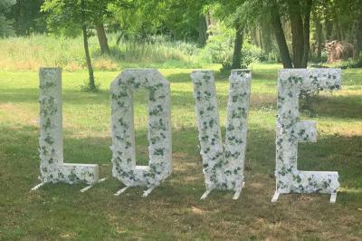 Salle décorée pour un événement, avec des tables rondes dressées, chaises rouges et un fond floral rose.