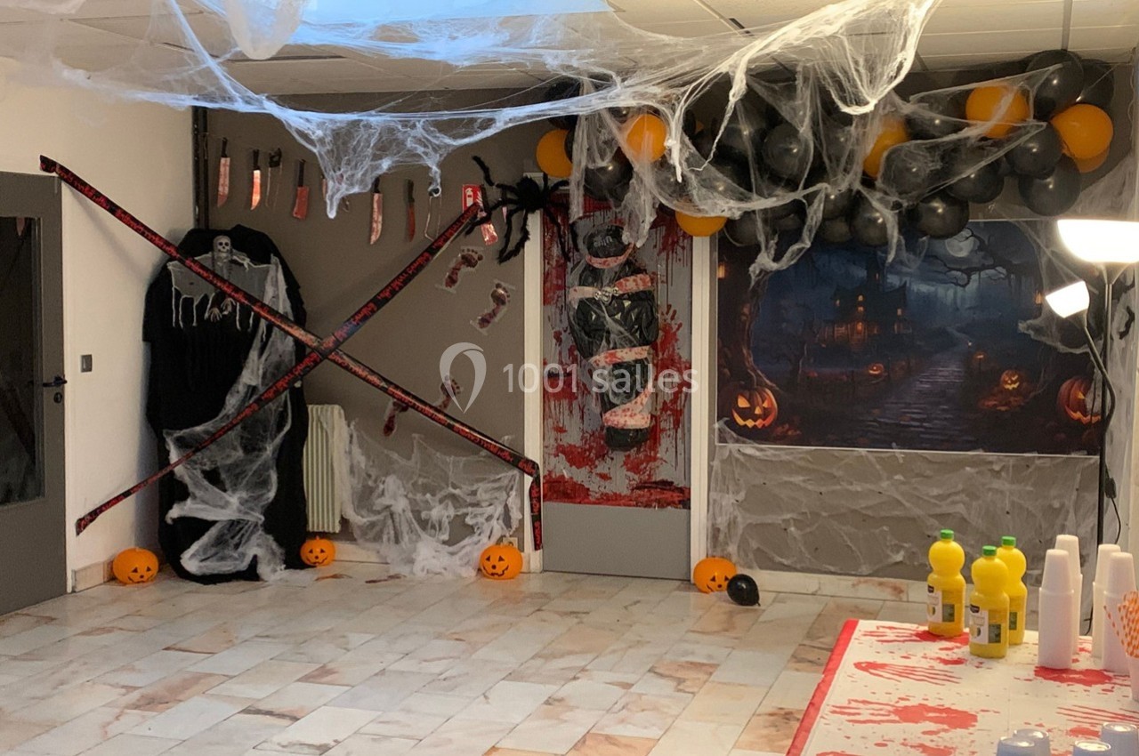 Salle décorée pour Halloween avec toiles d'araignée, ballons noirs et oranges, citrouilles et éléments effrayants.
