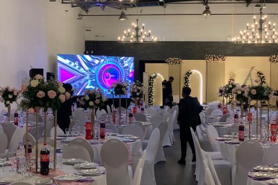 Salle décorée avec des tables rondes, nappes blanches et chaises rouges, prête pour un événement festif.