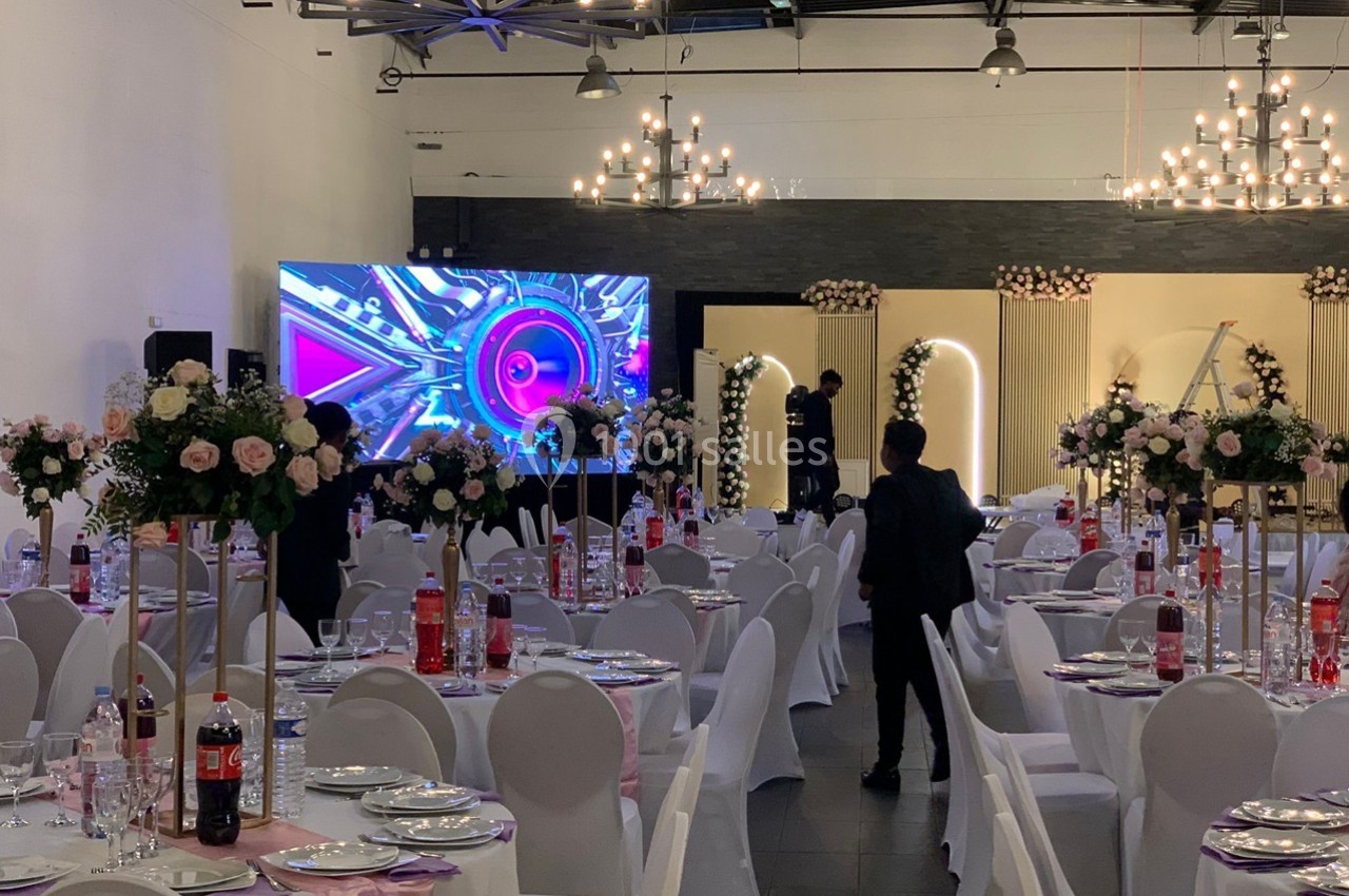 Salle de réception décorée avec des tables dressées, des fleurs et un écran géant affichant des graphismes colorés.