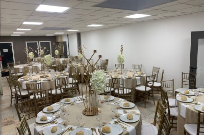 Salle décorée avec des tables rondes, nappes blanches et chaises rouges, prête pour un événement festif.
