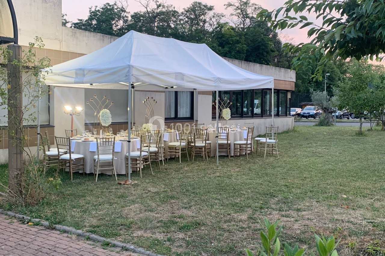 Tente blanche installée dans un jardin, abritant des tables décorées pour un événement en extérieur.