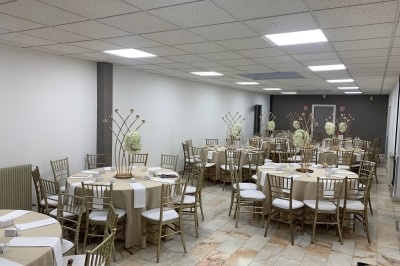 Salle décorée avec des tables rondes, nappes blanches et chaises rouges, prête pour un événement festif.