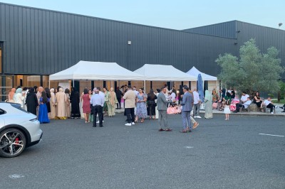 Salle décorée avec des tables rondes, nappes blanches et chaises rouges, prête pour un événement festif.