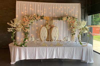 Salle décorée avec des tables rondes, nappes blanches et chaises rouges, prête pour un événement festif.