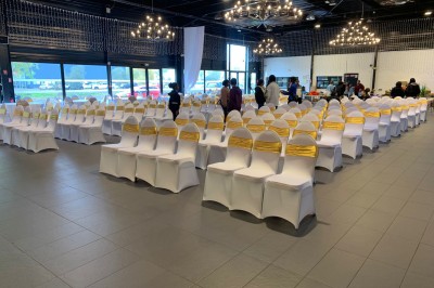Salle décorée avec des tables rondes, nappes blanches et chaises rouges, prête pour un événement festif.
