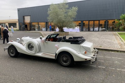 Salle décorée avec des tables rondes, nappes blanches et chaises rouges, prête pour un événement festif.