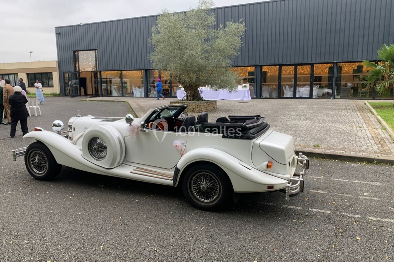 Voiture ancienne blanche décapotable garée devant un bâtiment moderne avec des baies vitrées.