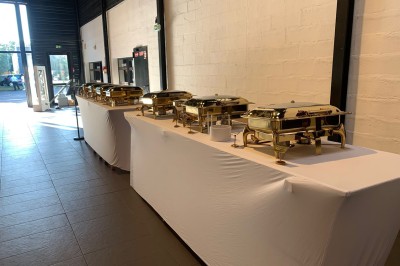 Salle décorée avec des tables rondes, nappes blanches et chaises rouges, prête pour un événement festif.