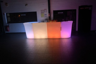 Salle décorée avec des tables rondes, nappes blanches et chaises rouges, prête pour un événement festif.