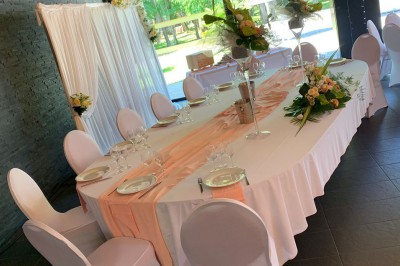 Salle décorée avec des tables rondes, nappes blanches et chaises rouges, prête pour un événement festif.