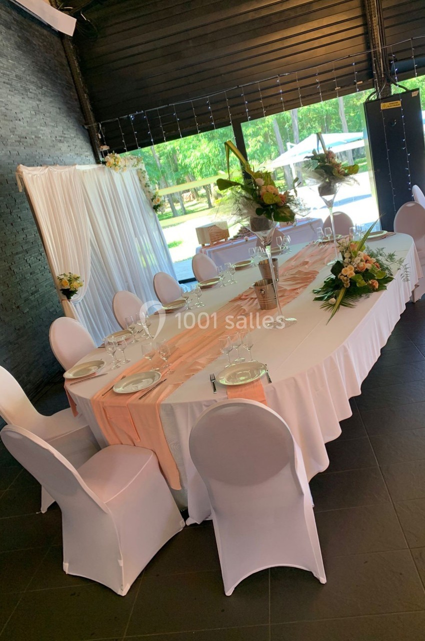 Table décorée pour un événement avec nappes blanches, chemins de table roses, chaises houssées et compositions florales.
