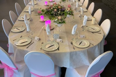 Salle décorée avec des tables rondes, nappes blanches et chaises rouges, prête pour un événement festif.