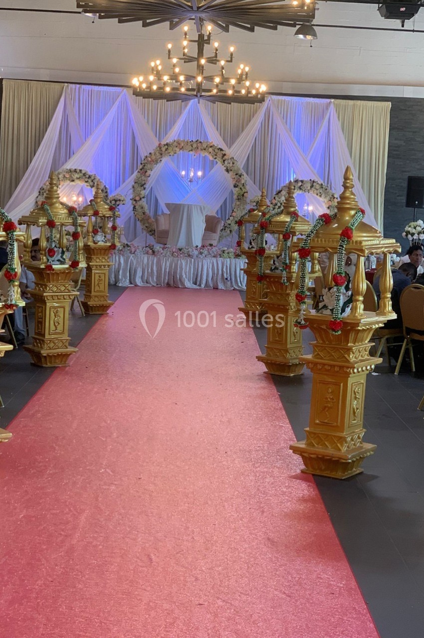 Allée décorée de lanternes dorées menant à une scène ornée de rideaux blancs et d'un arc floral lumineux.