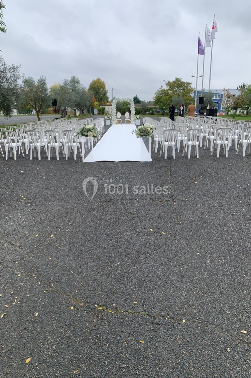 Allée centrale blanche entourée de chaises blanches disposées pour une cérémonie en extérieur par temps nuageux.