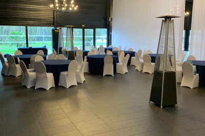 Salle décorée avec des tables rondes, nappes blanches et chaises rouges, prête pour un événement festif.