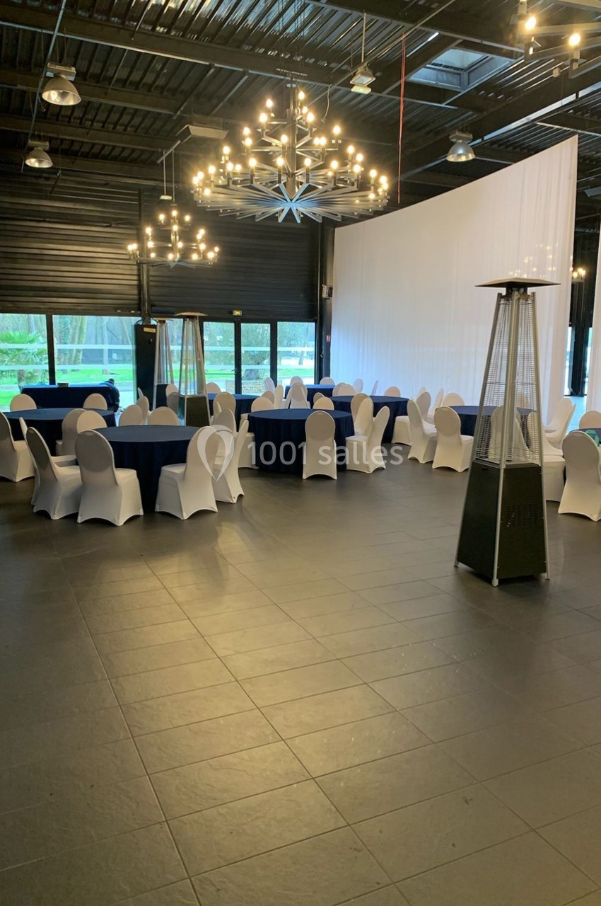 Salle de réception avec tables rondes nappées de bleu, chaises blanches et lustres modernes suspendus.