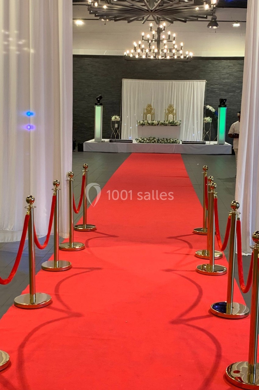 Allée avec tapis rouge bordée de poteaux dorés menant à une scène décorée pour un événement formel.