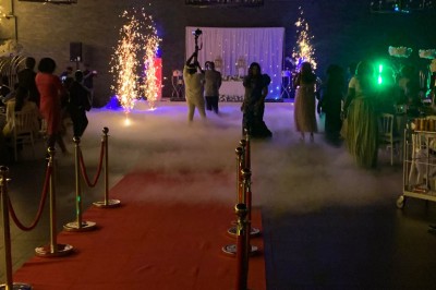 Salle décorée avec des tables rondes, nappes blanches et chaises rouges, prête pour un événement festif.