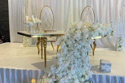 Salle décorée avec des tables rondes, nappes blanches et chaises rouges, prête pour un événement festif.
