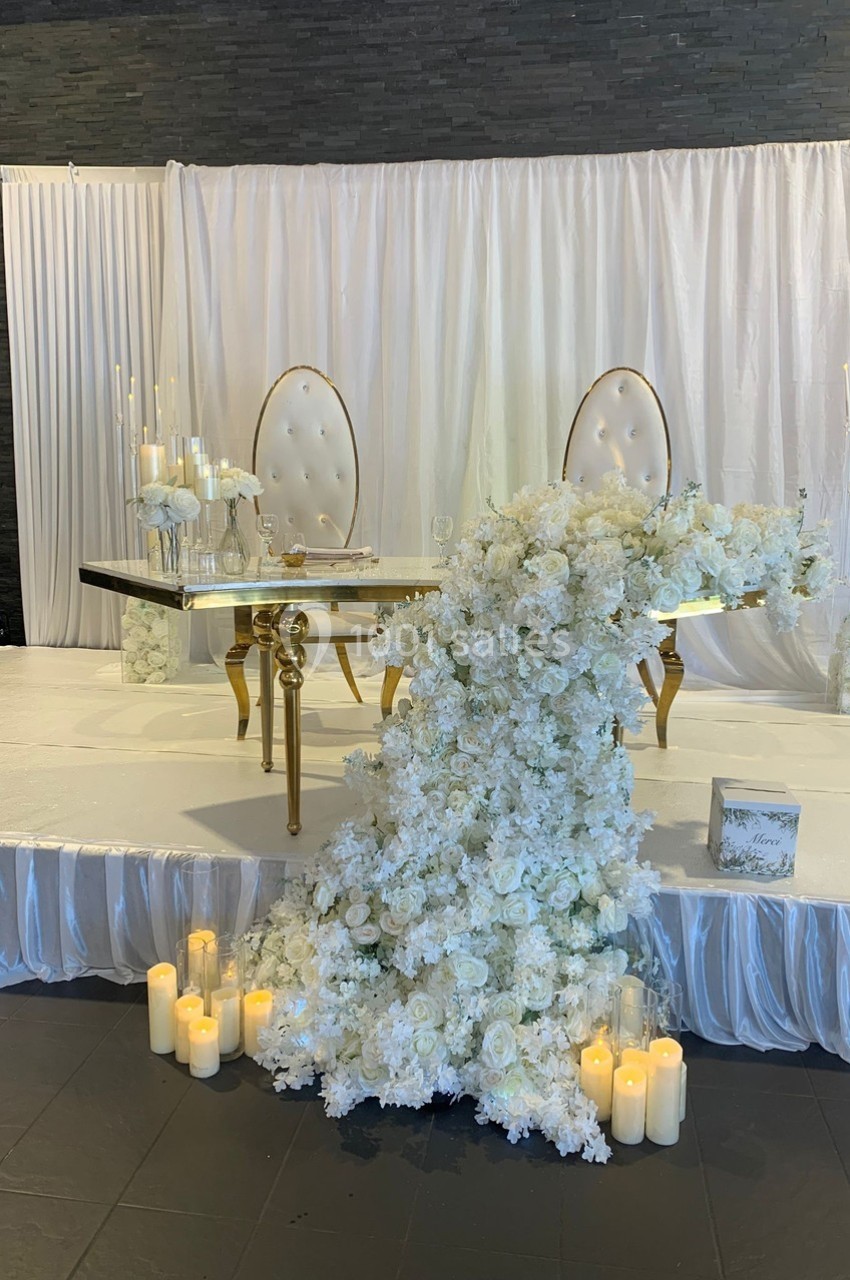 Table décorée pour un mariage avec chaises élégantes, cascade de fleurs blanches et bougies disposées au sol.